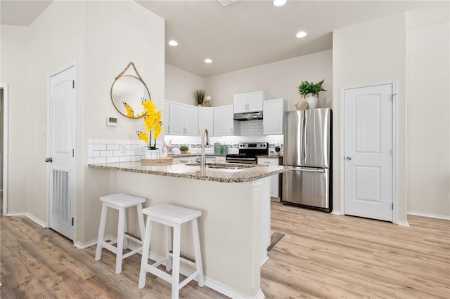 kitchen with light stone countertops, a peninsula, stainless steel appliances, white cabinets, and under cabinet range hood