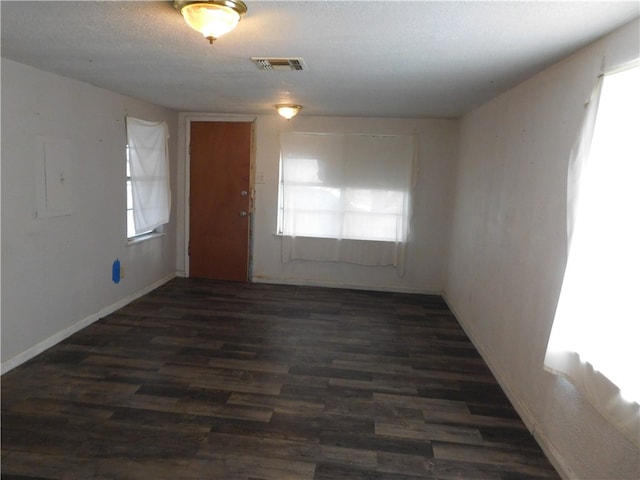 spare room with a wealth of natural light, a textured ceiling, and dark hardwood / wood-style floors