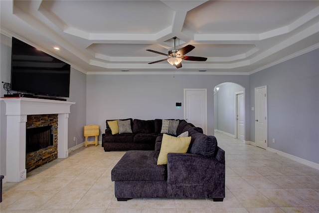 living room featuring light tile patterned flooring, ornamental molding, ceiling fan, a stone fireplace, and a raised ceiling