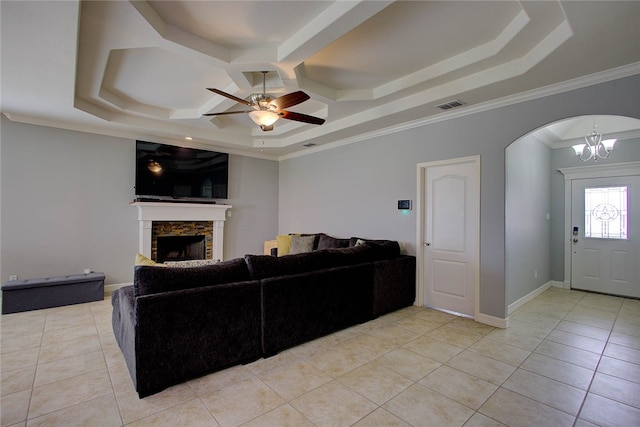 living room featuring a stone fireplace, a tray ceiling, light tile patterned floors, and crown molding