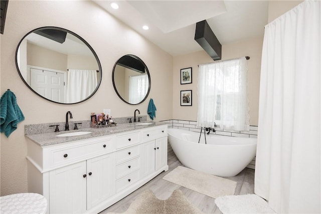 bathroom with vanity, a bath, and wood-type flooring