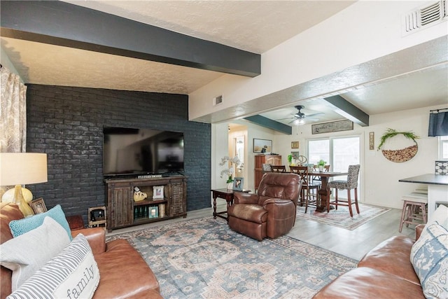 living room featuring vaulted ceiling with beams, a textured ceiling, hardwood / wood-style flooring, ceiling fan, and brick wall