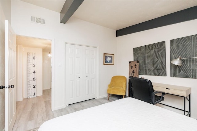 bedroom with beam ceiling, a closet, and light wood-type flooring