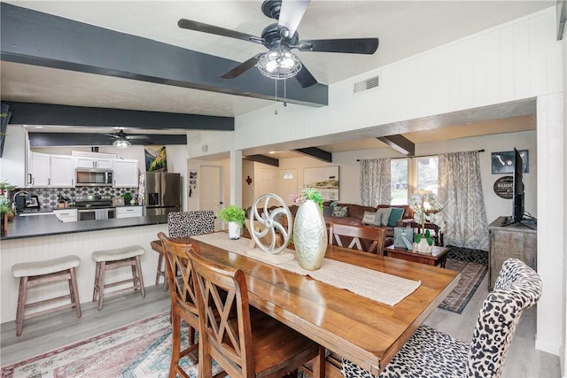 dining area featuring ceiling fan, light wood-type flooring, sink, and beam ceiling