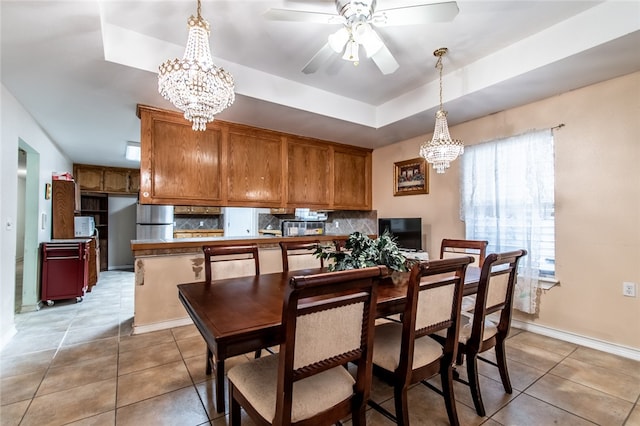 dining space with ceiling fan with notable chandelier, light tile patterned flooring, and a raised ceiling