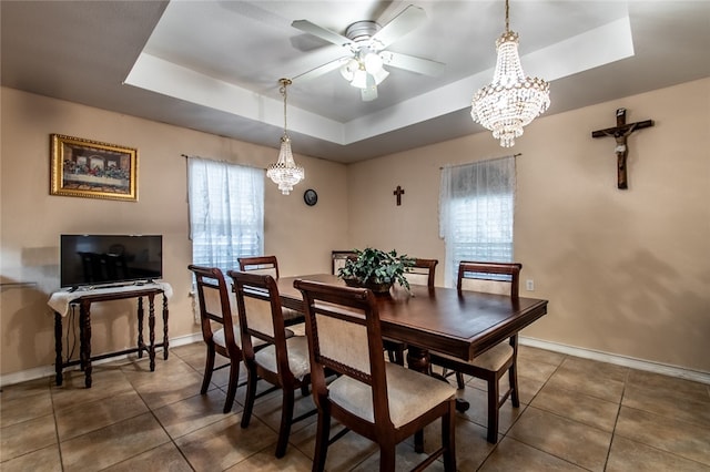 dining space featuring ceiling fan with notable chandelier, dark tile patterned floors, and a tray ceiling