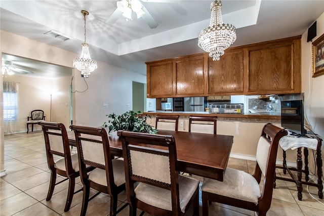 tiled dining space featuring a raised ceiling and ceiling fan with notable chandelier