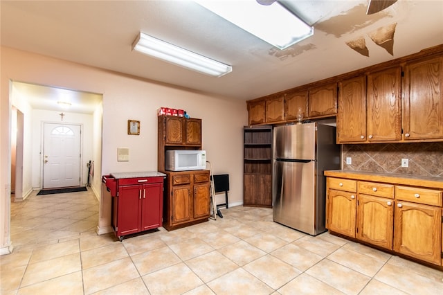 kitchen featuring stainless steel refrigerator, light tile patterned floors, and tasteful backsplash