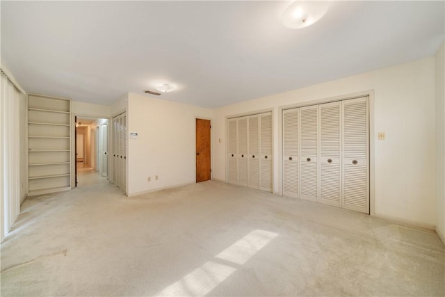 unfurnished bedroom with multiple closets and light carpet