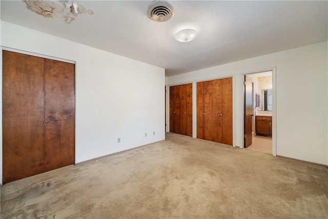 unfurnished bedroom featuring light colored carpet, multiple closets, and ensuite bathroom