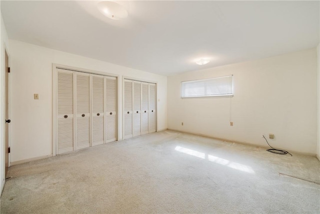 unfurnished bedroom featuring multiple closets, lofted ceiling, and light colored carpet