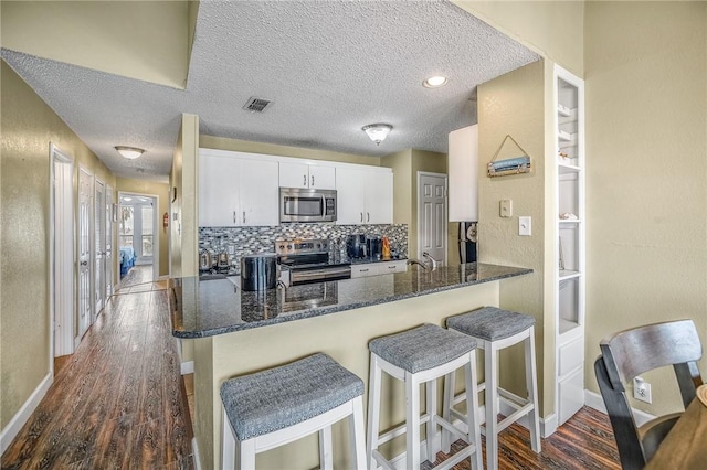 kitchen with white cabinets, dark stone countertops, kitchen peninsula, and appliances with stainless steel finishes