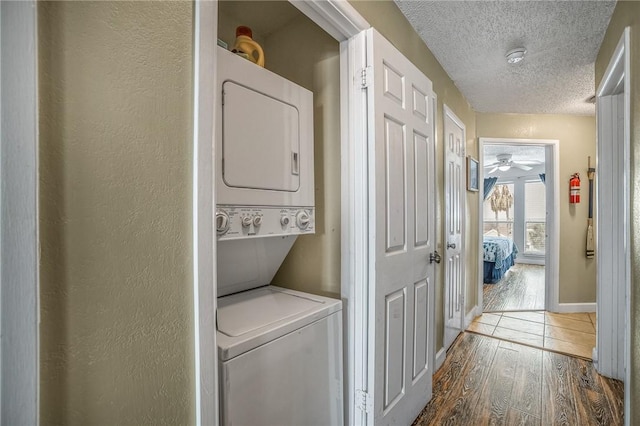 washroom with a textured ceiling, stacked washer / dryer, and dark hardwood / wood-style flooring