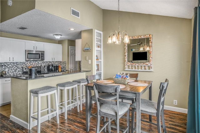 dining area featuring an inviting chandelier, a textured ceiling, dark hardwood / wood-style floors, and vaulted ceiling