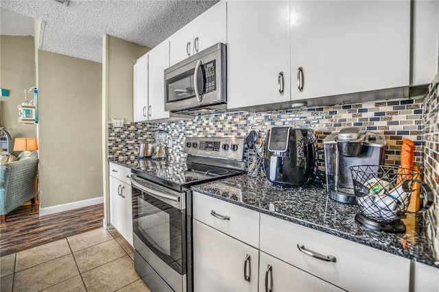 kitchen featuring white cabinets, light tile patterned floors, a textured ceiling, dark stone countertops, and stainless steel appliances