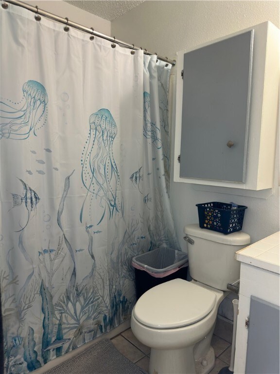 bathroom featuring toilet, vanity, a textured ceiling, and tile patterned floors