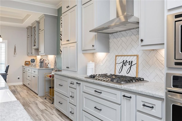 6401 Kobe Dr, Corpus Christi, TX 78414 - kitchen featuring wall chimney range hood, stainless steel appliances, tasteful backsplash, ornamental molding, and light wood-style floors