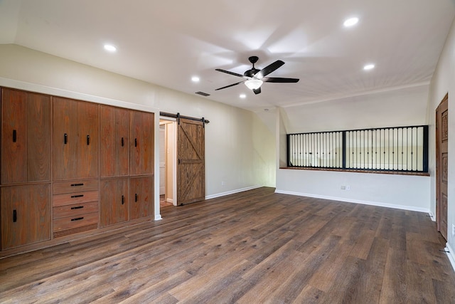 unfurnished living room featuring a barn door, ceiling fan, dark wood-type flooring, and vaulted ceiling