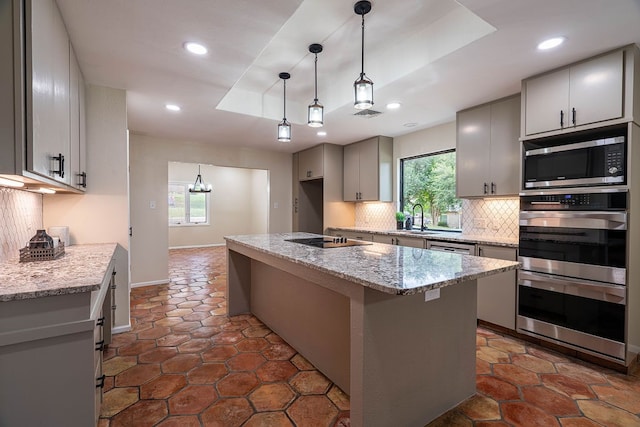 kitchen with a raised ceiling, light stone counters, and an island with sink