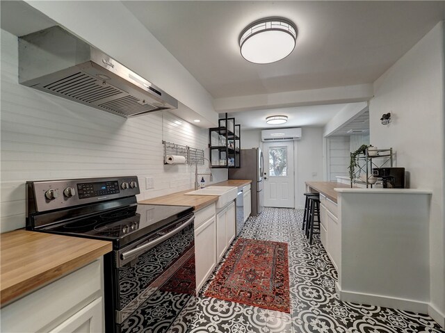 kitchen with butcher block counters, white cabinetry, appliances with stainless steel finishes, wall chimney exhaust hood, and a wall mounted AC