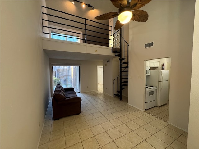 living room featuring light tile patterned floors, ceiling fan, and a towering ceiling