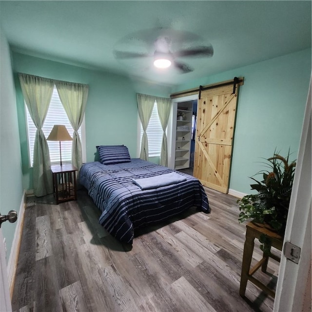 bedroom with a barn door, hardwood / wood-style flooring, and ceiling fan