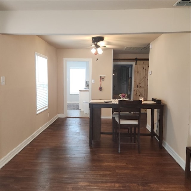 dining area with dark wood-type flooring, a barn door, and ceiling fan