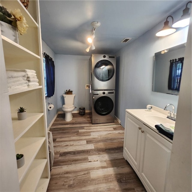 bathroom with toilet, vanity, hardwood / wood-style flooring, and stacked washer / drying machine