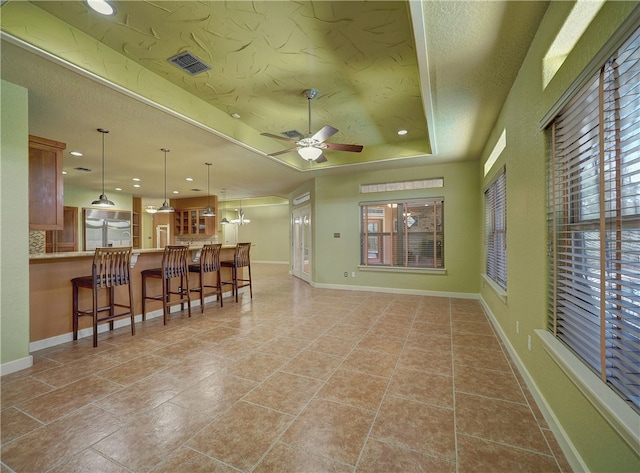 living room with ceiling fan with notable chandelier, a textured ceiling, a tray ceiling, and light tile patterned floors