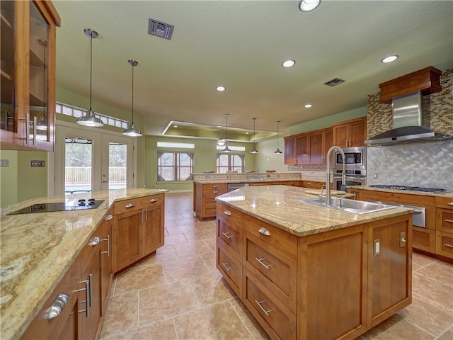 kitchen featuring stainless steel appliances, wall chimney exhaust hood, decorative light fixtures, an island with sink, and decorative backsplash