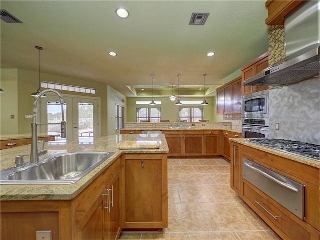 kitchen featuring stainless steel appliances, wall chimney exhaust hood, hanging light fixtures, sink, and tasteful backsplash