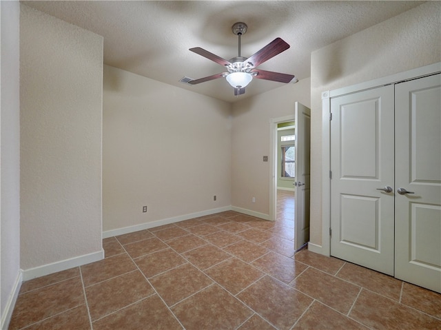 empty room with a textured ceiling, ceiling fan, and light tile patterned flooring