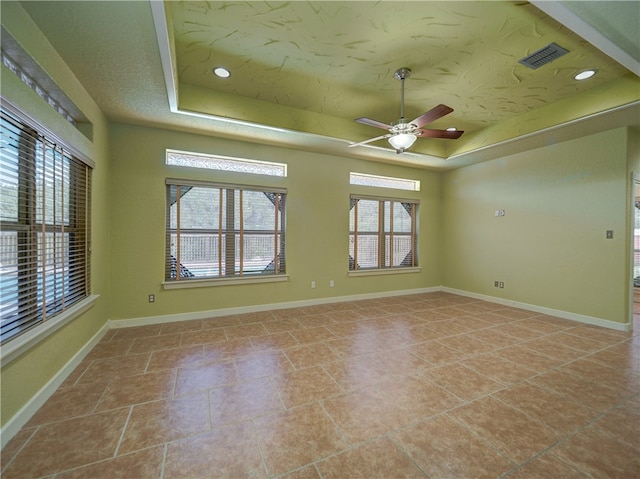 empty room featuring light tile patterned flooring, ceiling fan, a textured ceiling, and a tray ceiling