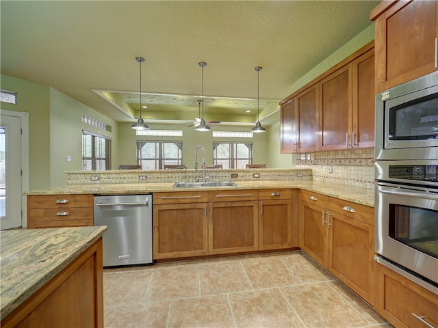 kitchen featuring stainless steel appliances, light stone countertops, hanging light fixtures, and sink