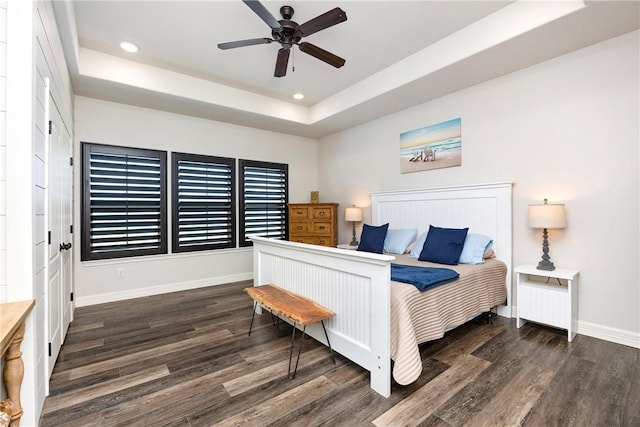 bedroom with ceiling fan, dark hardwood / wood-style flooring, and a tray ceiling