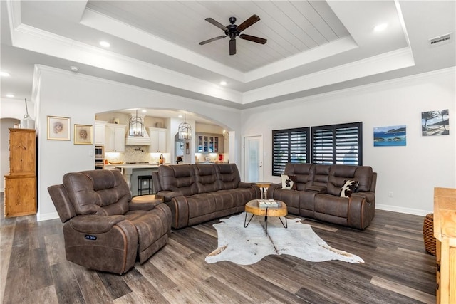 living room featuring a raised ceiling, dark wood-type flooring, ceiling fan with notable chandelier, and ornamental molding