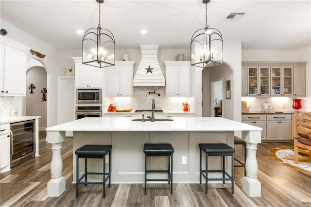 kitchen featuring a large island with sink, hanging light fixtures, stainless steel appliances, and wine cooler