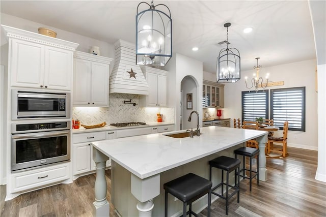 kitchen featuring a large island with sink, hanging light fixtures, light stone counters, white cabinetry, and stainless steel appliances