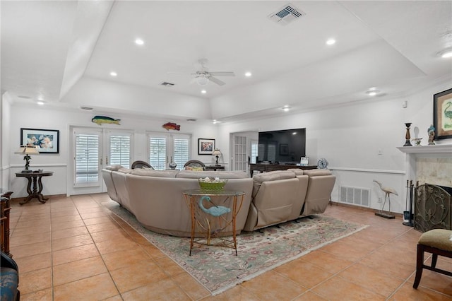 tiled living room featuring french doors, ceiling fan, and a raised ceiling