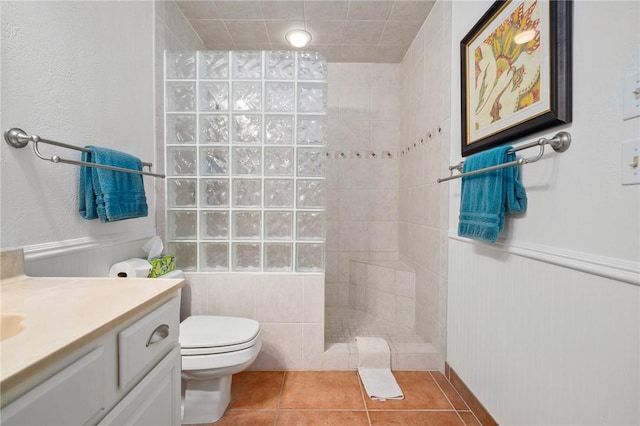 bathroom with toilet, vanity, a tile shower, and tile patterned flooring