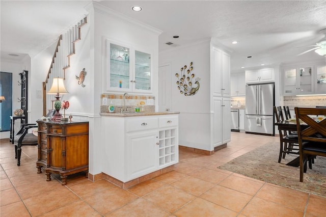 kitchen with tasteful backsplash, crown molding, white cabinetry, stainless steel appliances, and light tile patterned floors