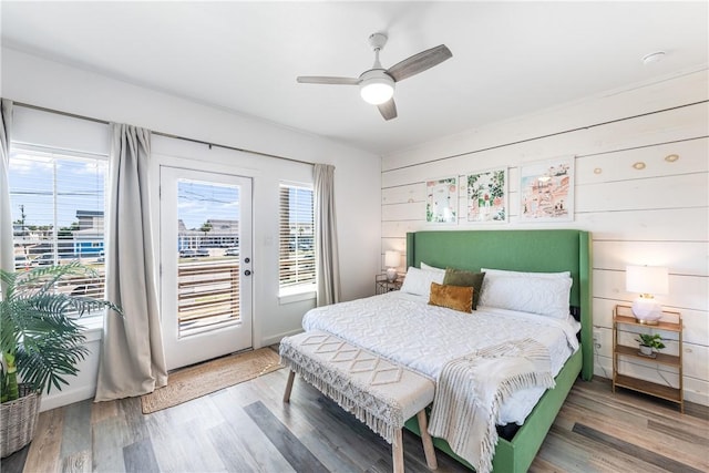 bedroom with hardwood / wood-style floors, ceiling fan, wooden walls, and access to outside