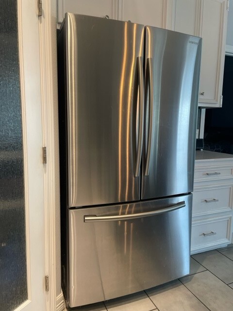 kitchen with white cabinets, light tile patterned floors, and stainless steel fridge