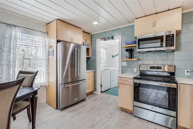 kitchen with light brown cabinetry, decorative backsplash, washing machine and dryer, and appliances with stainless steel finishes