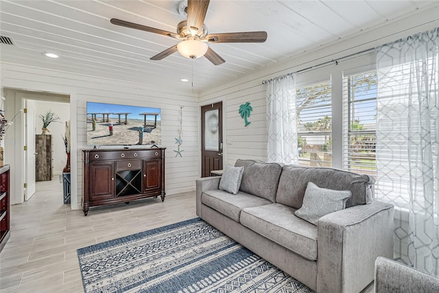 living room with wooden walls, ceiling fan, and light hardwood / wood-style floors