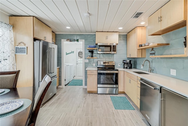 kitchen with appliances with stainless steel finishes, washer and clothes dryer, sink, and light brown cabinets