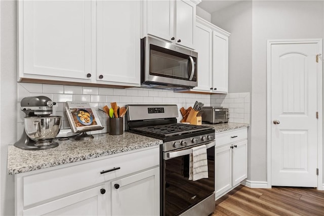 kitchen with appliances with stainless steel finishes, hardwood / wood-style floors, light stone counters, white cabinets, and decorative backsplash