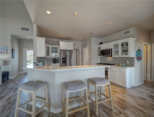 kitchen with white cabinetry, light wood-type flooring, a kitchen breakfast bar, stainless steel appliances, and decorative backsplash