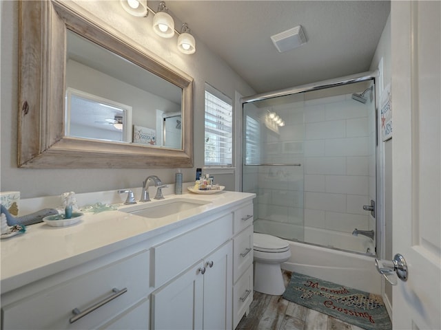 full bathroom with hardwood / wood-style floors, bath / shower combo with glass door, vanity, a textured ceiling, and toilet