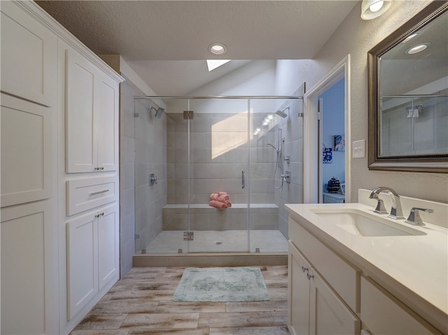 bathroom featuring hardwood / wood-style floors, vaulted ceiling with skylight, a shower with shower door, vanity, and a textured ceiling